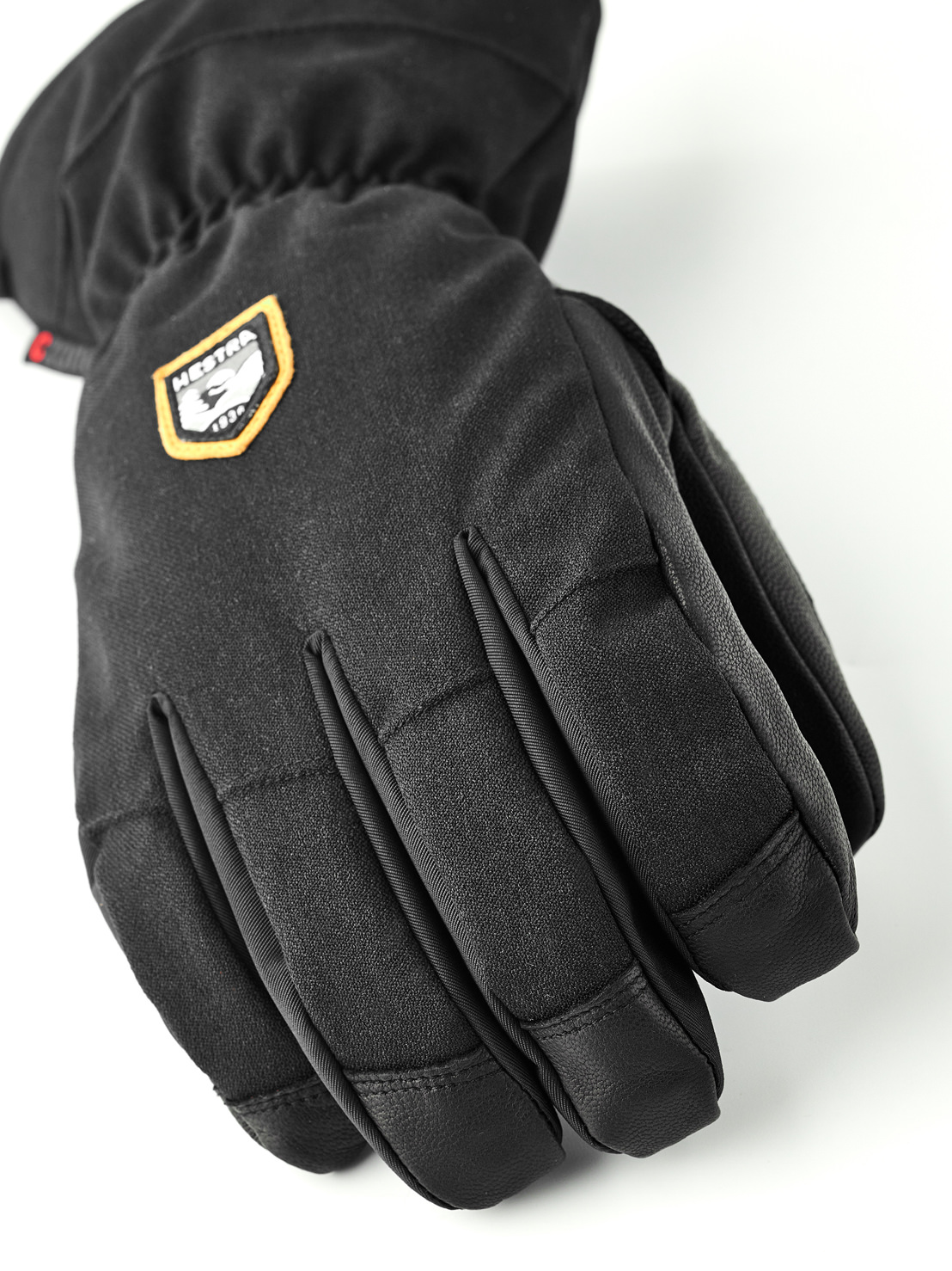 Gant noir à cinq doigts Gros plan sur un gant noir à cinq doigts avec le logo Hestra sur le dos de la main.