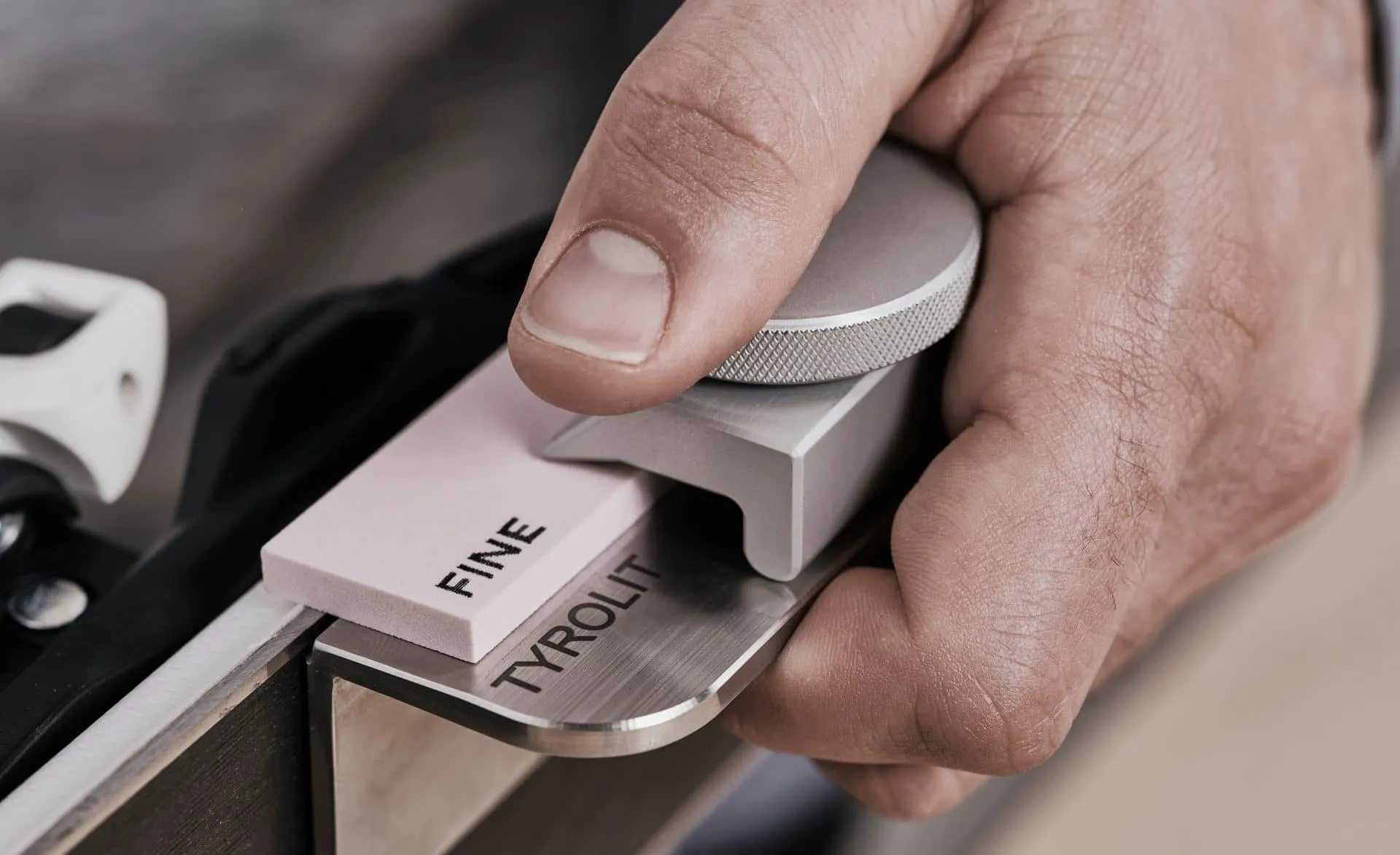 Primo piano: una mano affila la lamina di uno sci con una pietra per affilare di Tyrolit e un utensile per affilare.