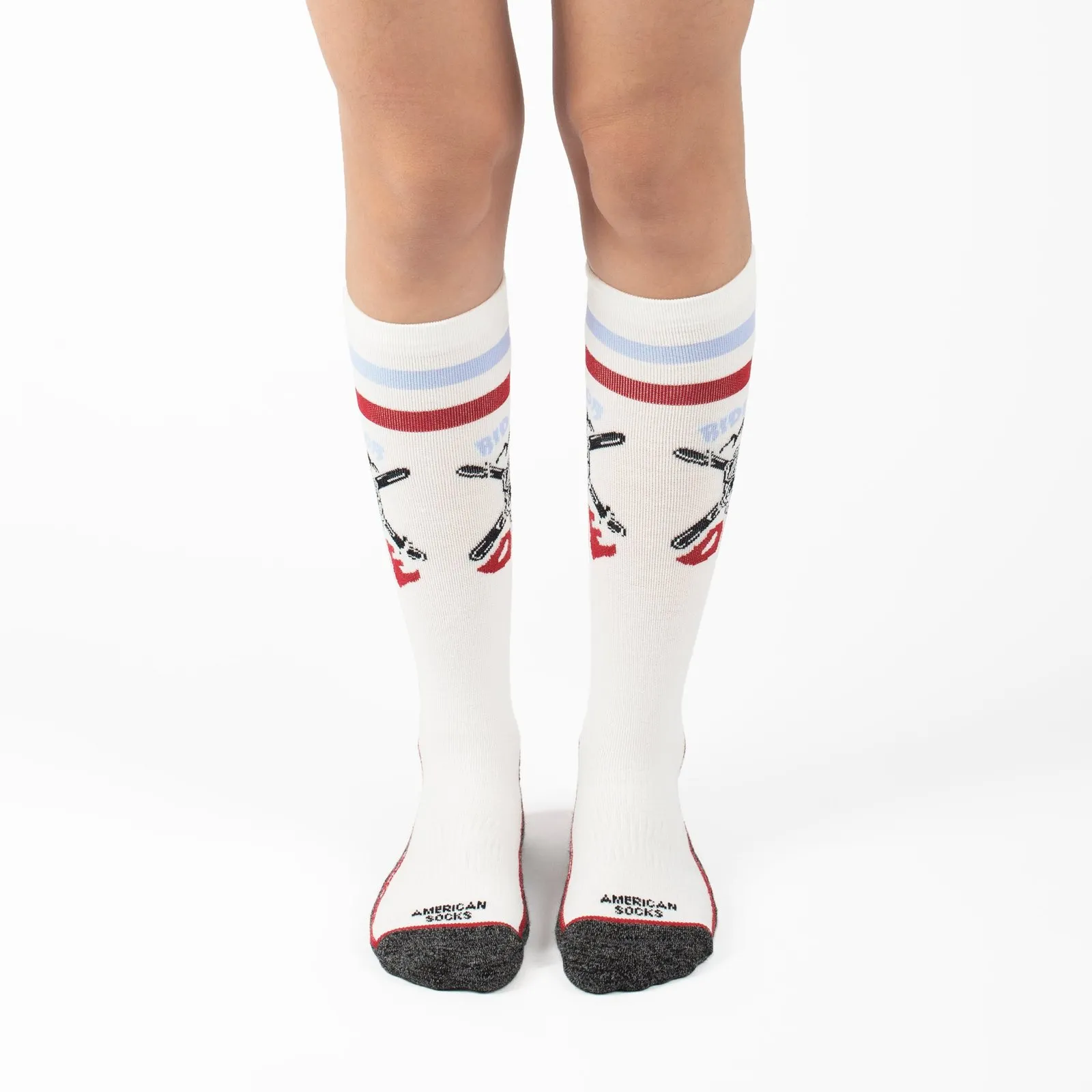 Gambe con calze da neve bianche alte fino al ginocchio, design con snowboard incrociati e strisce rosso/blu. Scritta "Ride or Die".