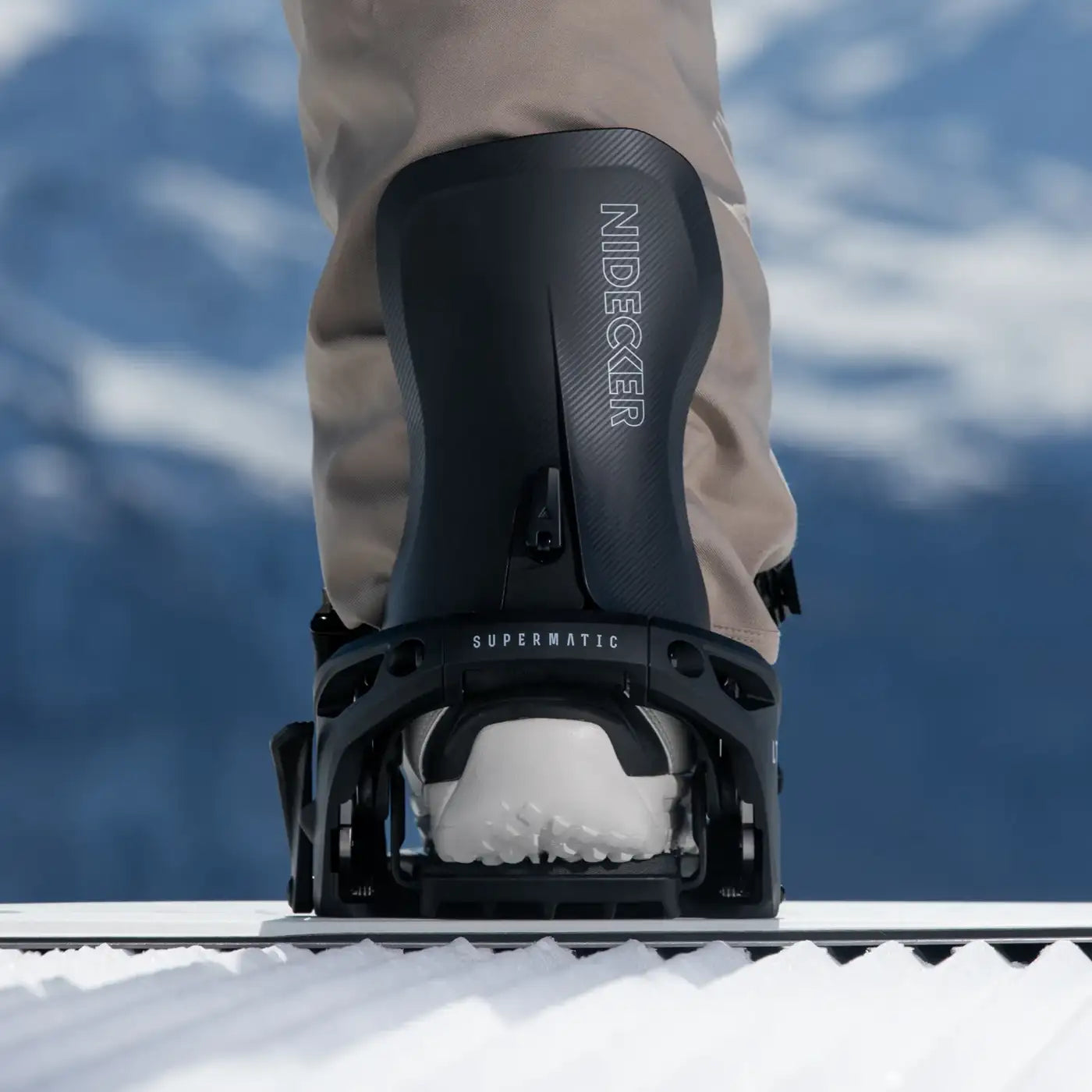 Gros plan sur une fixation de snowboard "Nidecker Supermatic " avec une botte sur un snowboard dans la neige sur un fond flou.