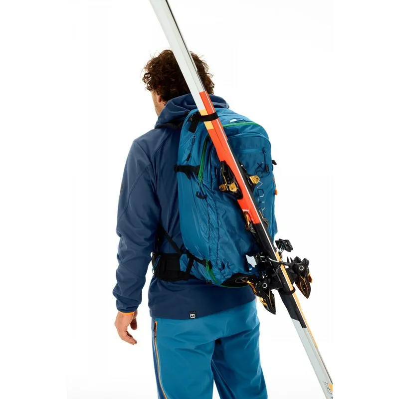 Persona con zaino Ortovox Ascent 32 blu e sci in spalla.