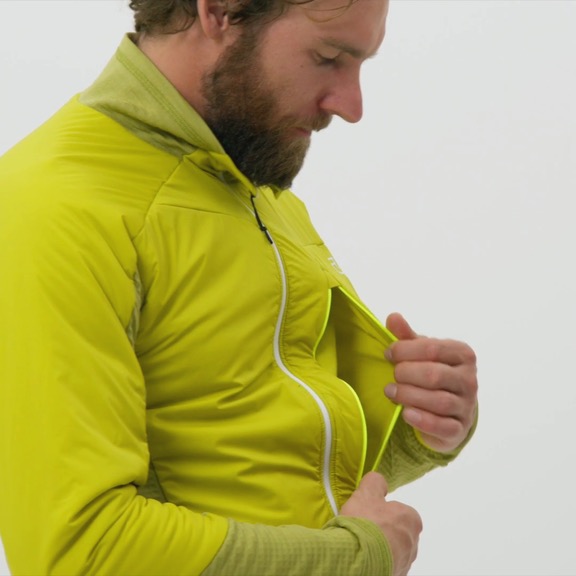 Ein Mann mit Bart öffnet eine hellgrüne Hybrid Jacke, die mit Swisswool isoliert ist.