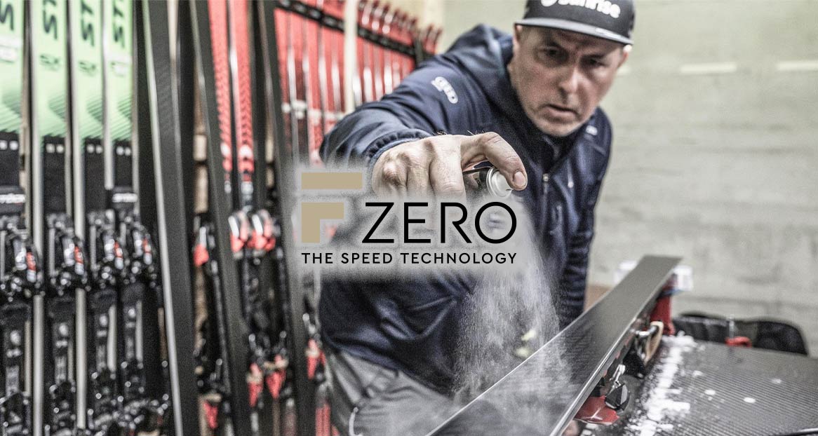 Un homme vaporise du fart sur un ski, à côté du logo "F Zero - The Speed Technology" et d'autres skis.