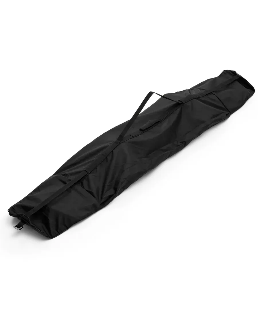 Black, empty snowboard bag made of nylon fabric with carrying strap lies diagonally on a light background.