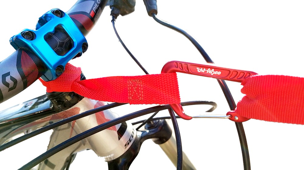 Nahaufnahme eines Fahrradlenkers mit blauem Vorbau und roter Tow-Whee Quick Loop-Schlaufe mit Karabiner befestigt.