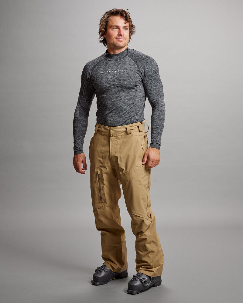 Mann in Skiausrüstung Ein Mann, der eine sandfarbene Y-1 HD GORE-TEX Pro 3L Shell Hose und ein graues Shirt trägt. Er trägt Skischuhe.