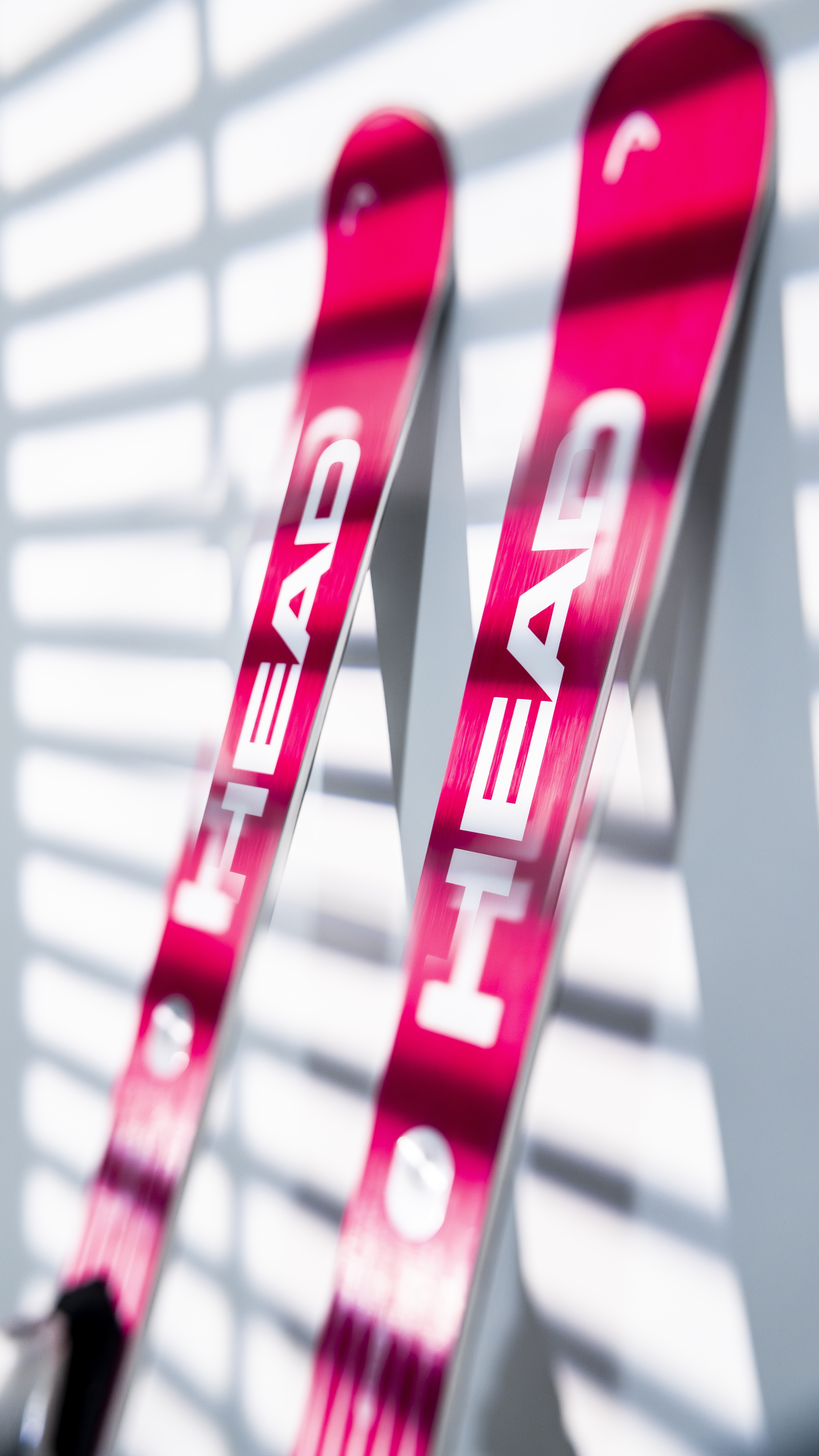 Pinkfarbene Head Ski Zwei pinkfarbene Head Ski, mit weißer Schrift, lehnen an einer hellen Wand mit Schattenlinien.