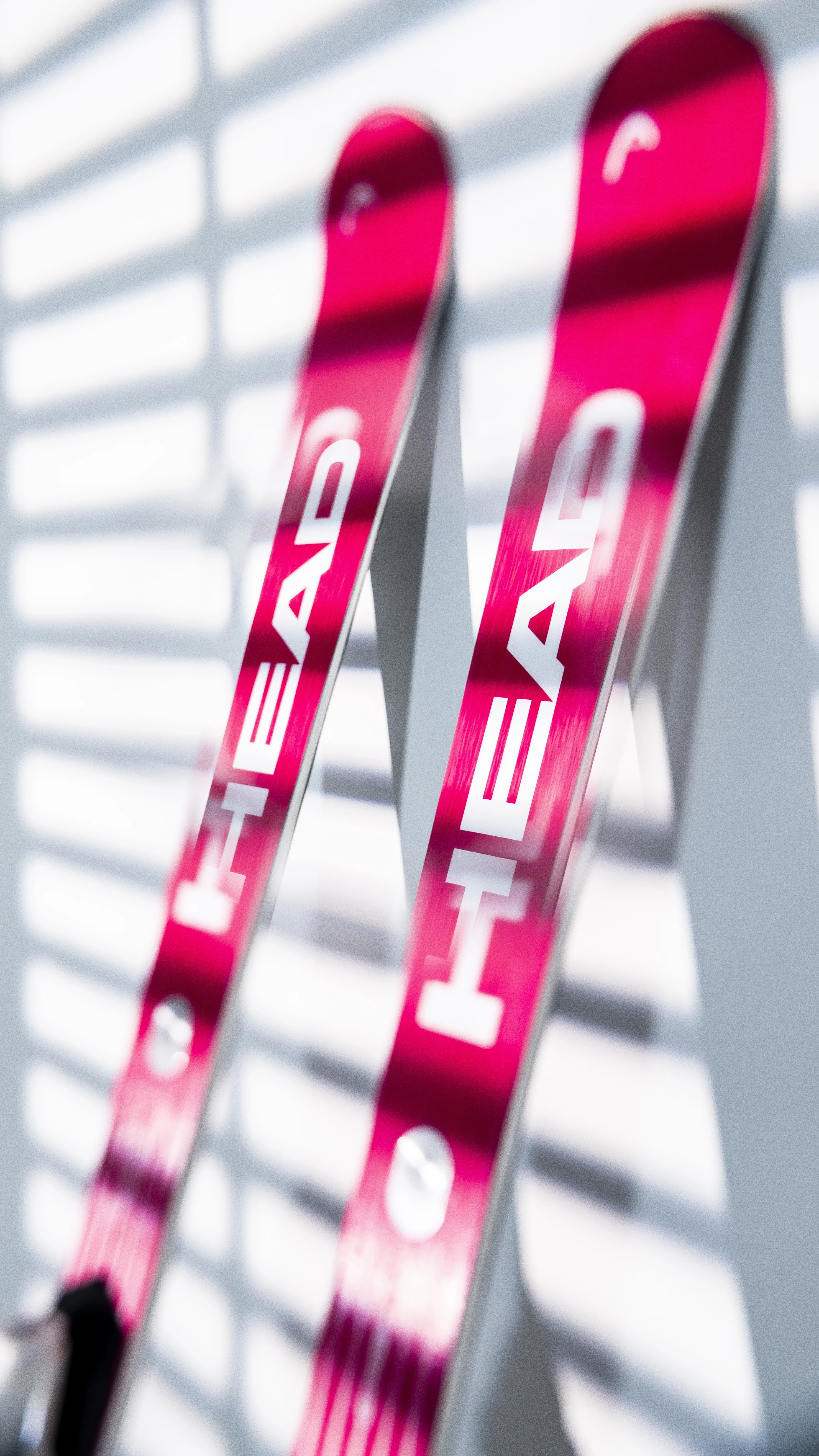 Zwei pinkfarbene Head Ski, mit weißer Schrift, lehnen an einer hellen Wand mit Schattenlinien.