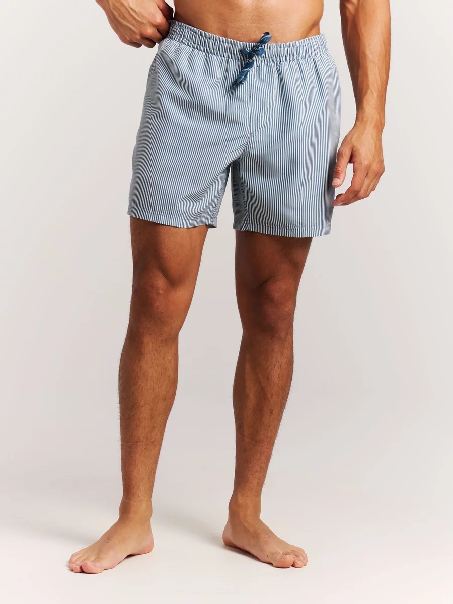 Ein Mann, von den Hüften abwärts zu sehen, trägt hellblaue, vertikal gestreifte Badeshorts mit Kordelzug.
