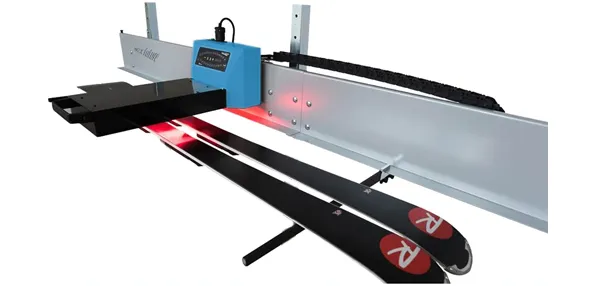 Due sci sotto il dispositivo di sciolinatura a infrarossi con luce rossa, unità di controllo blu e supporto grigio su sfondo bianco.