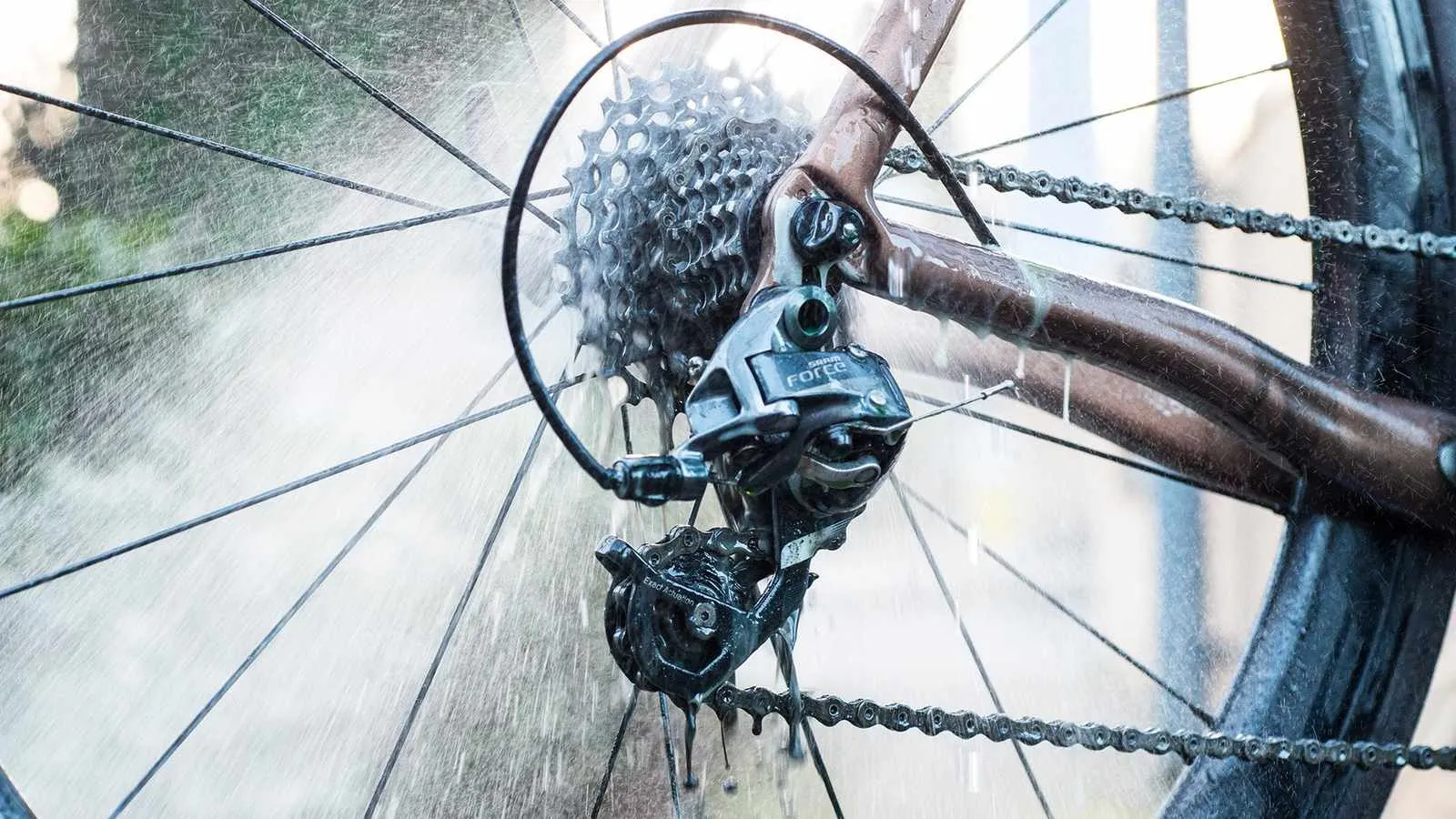 Nahaufnahme eines Fahrradantriebs unter Wasserstrahl. Kette, Kassette, Umwerfer sind sichtbar. Muc-Off Drivetrain Cleaner Anwendung.